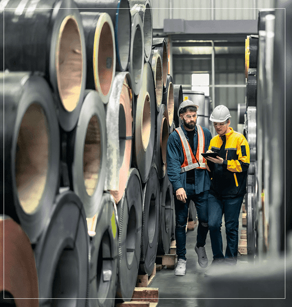 Workers inspecting metal rolls in warehouse.